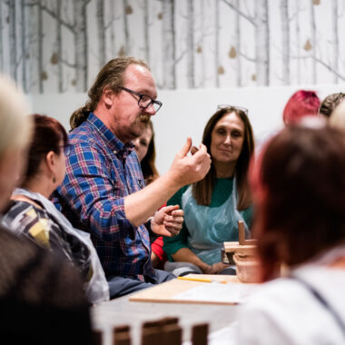 Peter Jones demonstrates how to make ceramic figures wearing a plaid shirt and glasses.