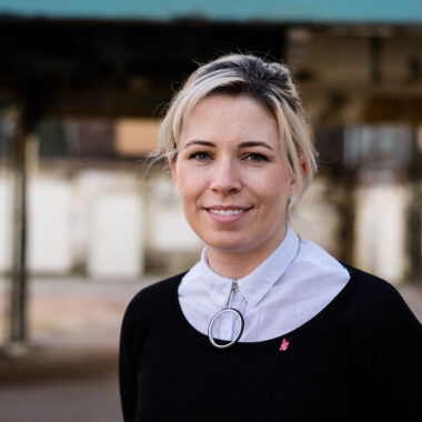 Natalie stands in front of Spode factory wearing a white shirt, black jumper and silver necklace.