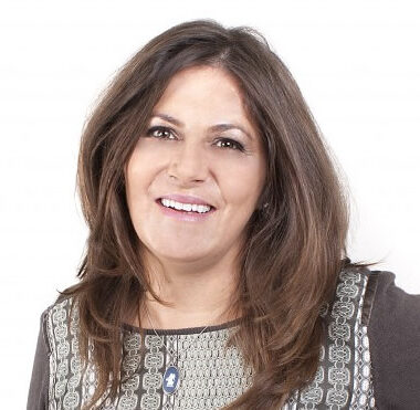 Alison Wedgwood stands against a white background with brown hair and a brown top on.