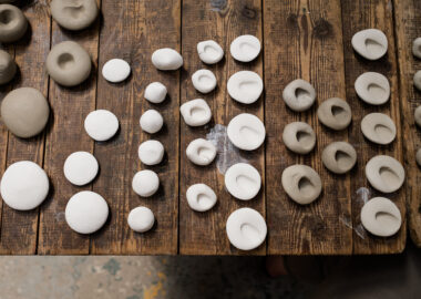 Rows of white and terracotta ceramic pebbles are lined up on a wooden table, varying in size.