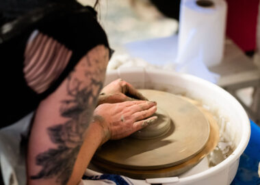 A person centres a lump of grey clay of a pottery wheel.