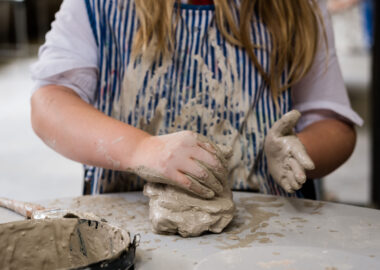 A child squishes clay between her hands on a grey table.