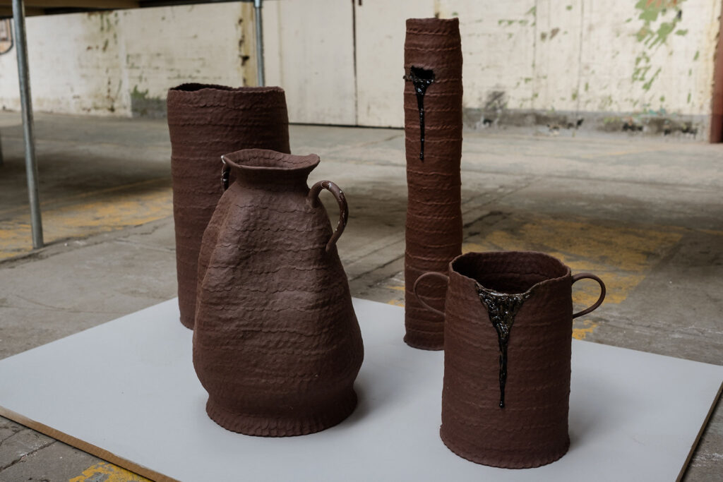 Coiled terracotta pots and vessels are exhibited on a grey plinth.