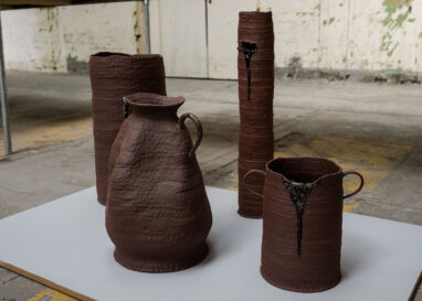 Coiled terracotta pots and vessels are exhibited on a grey plinth.