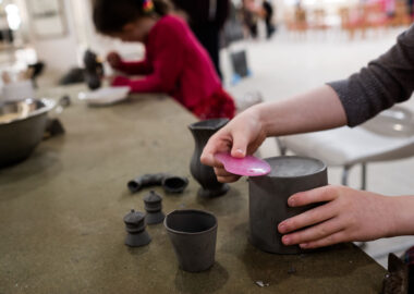 A person smooths the bottom of a pot with a pink plastic kidney tool.