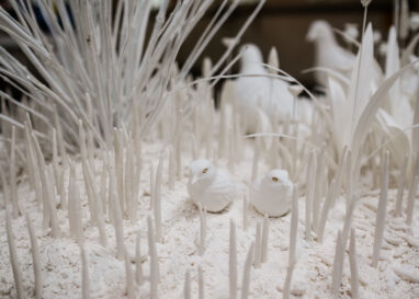 Two porcelain white birds sit atop white porcelain soil surrounded by white porcelain grass stems.