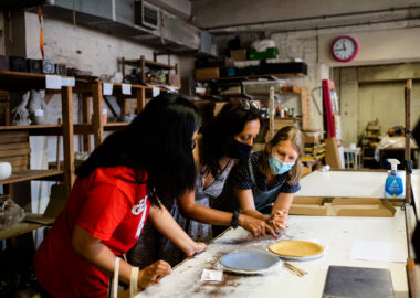 Three people work together to make plates in a ceramics studio.