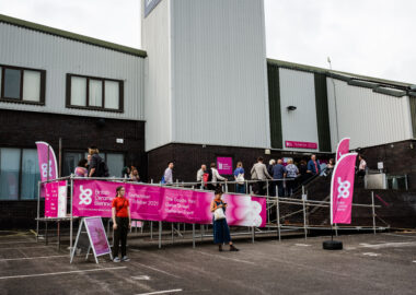 People queue up infront of a grey building, The Goods Yard, to get into BCB 2021 festival.