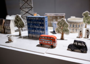 A ceramic cityscape installation with a red bus, apartment block and painted, ceramic trees.