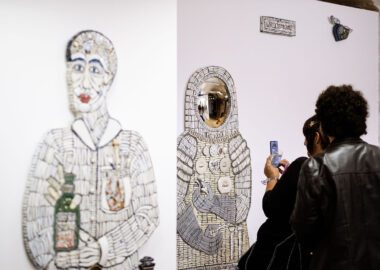 Two people dressed in black are photographing a life-size ceramic mosaic figure.