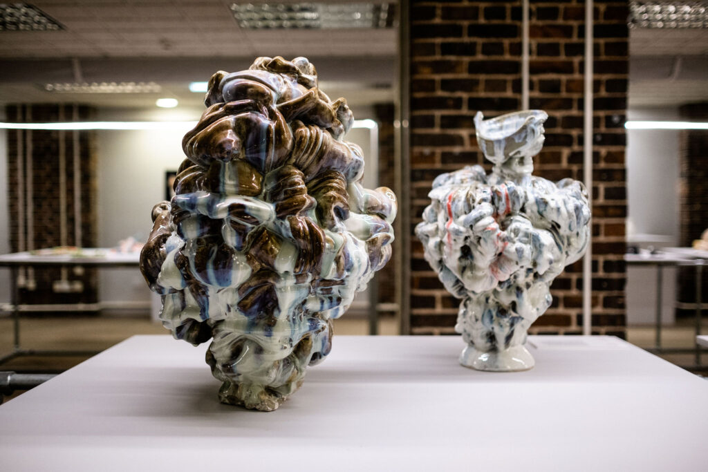 Two ceramic sculptures made up glazed ribbons of clay are displayed on a white plinth.