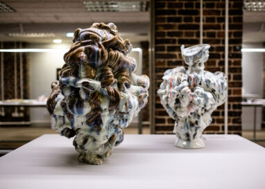 Two ceramic sculptures made up glazed ribbons of clay are displayed on a white plinth.