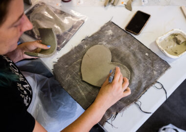 This image is to promote episode 1 of the Recast Podcast. A participant of the programme is working on a ceramic heart shape.