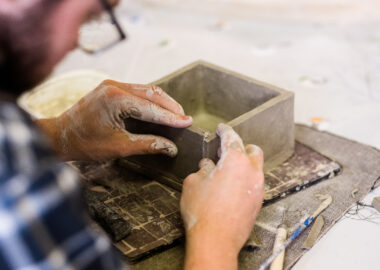 At the Recast headquarters at Stoke Recovery Service, a participant works on a box made with flat clay slabs, smoothing the surface. This image is to promote the Recast podcast.
