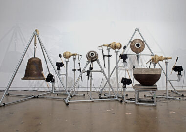 Ceramic forms that resemble instruments like drums, bells and maracas are suspended within metal frames. Sound equipment is wired to the forms.