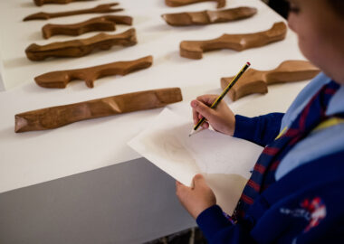 A child in a school uniform is drawing a ceramic piece displayed in front of them.