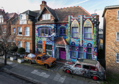 A house with two cars out front, all covered in brightly coloured ceramic tiles.