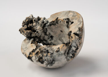 A hemisphere of clay, with parts missing as if eroded away, and rough textured growths on one side.