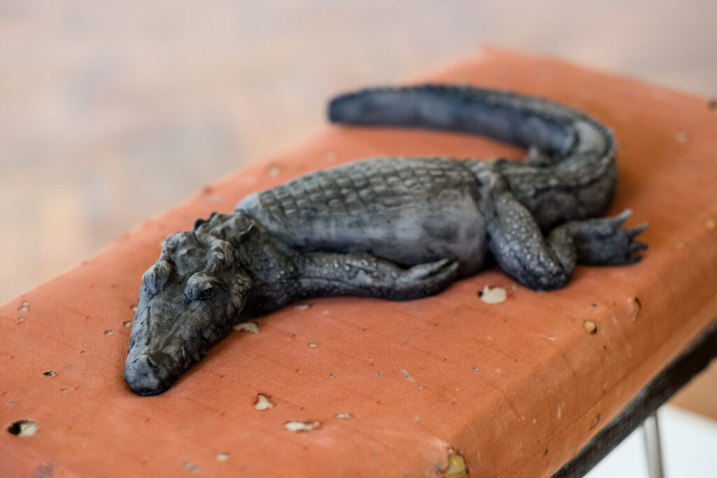 A clay crocodile lays on a fabric stool, as part of Dorcas Casey's work at the 2023 British Ceramics Biennial.