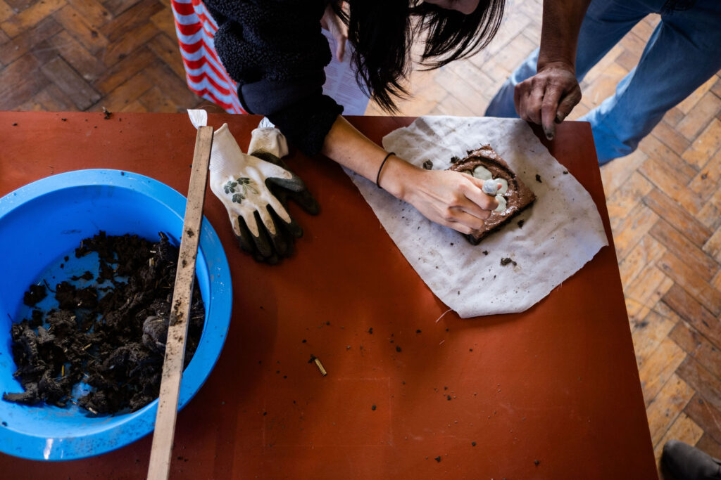 A person is squeezing clay slip onto a tile in the Tactile Project Space.