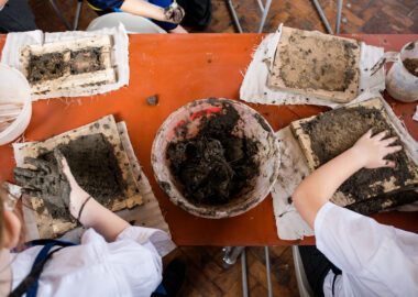 Looking from above, two children are pressing clay into wooden frames as part of a workshop in the Tactile Project Space.