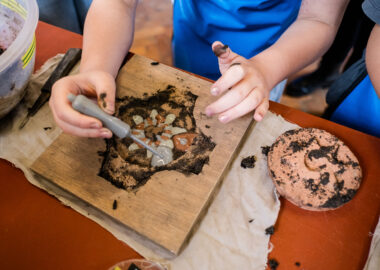 Close-up of a hand holding a pipette of clay slip and squeezing it into an indented pattern on a clay tile.