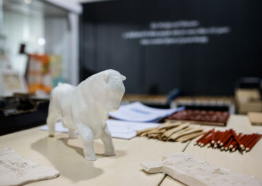 Ceramic figurine of a bull, surrounded by paper, pencils and other art materials.