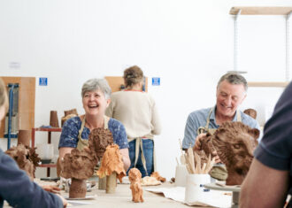 Visitors to Open Source laughing and smiling as they sculpt a clay lion head.